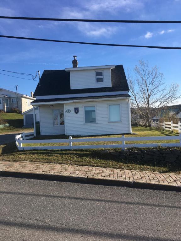 a white house with a black roof on a street at La petite maison sur la côte in Sainte-Anne-des-Monts