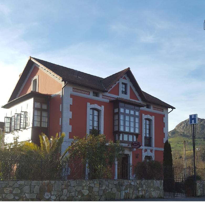 una casa roja y blanca con una colina al fondo en Hotel Asturias, en Arriondas