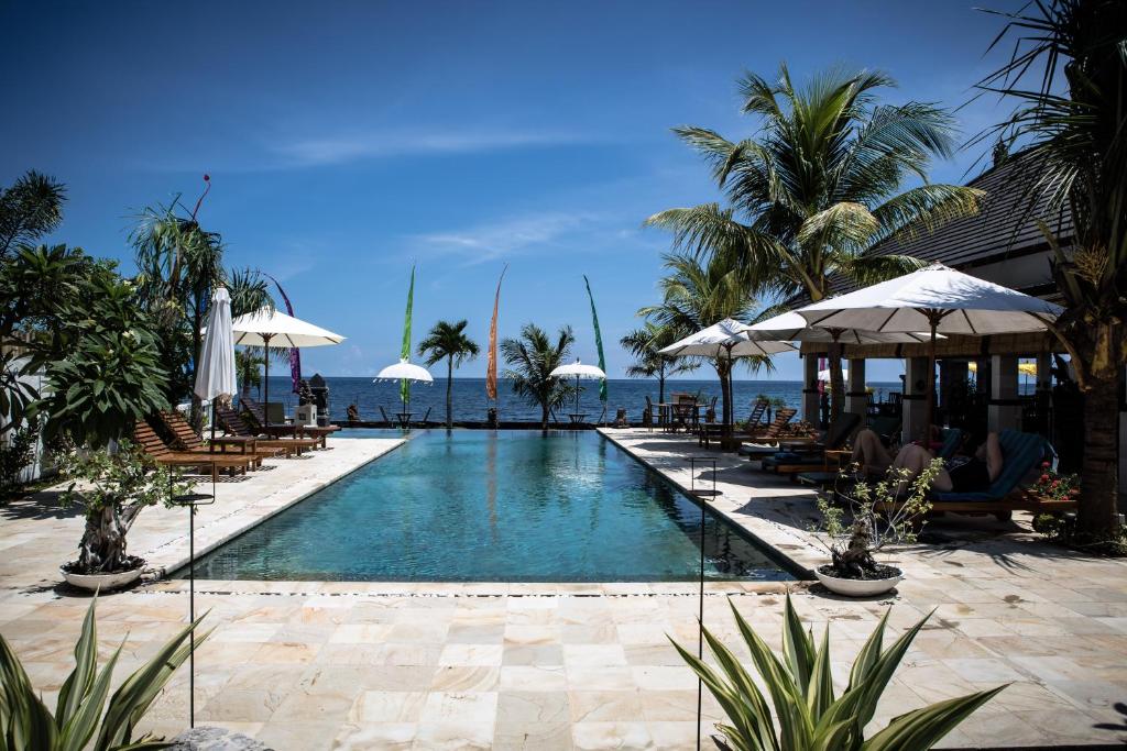 a swimming pool with chairs and umbrellas and the ocean at Kelapa Lovina Beach Villa in Lovina