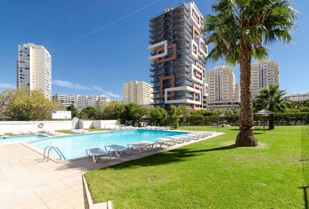 une piscine avec des chaises et un grand bâtiment dans l'établissement Praia da Rocha, Algarve Sunny Apartment, à Portimão