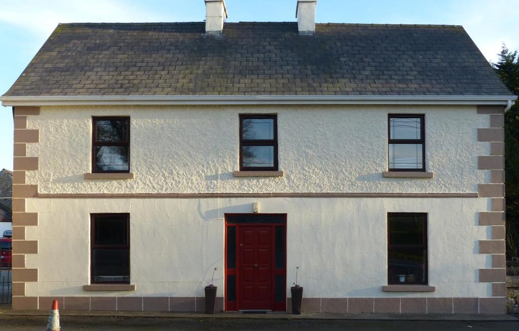 Casa blanca con puerta roja y ventanas en Garadice View Farm House, en Ballinamore