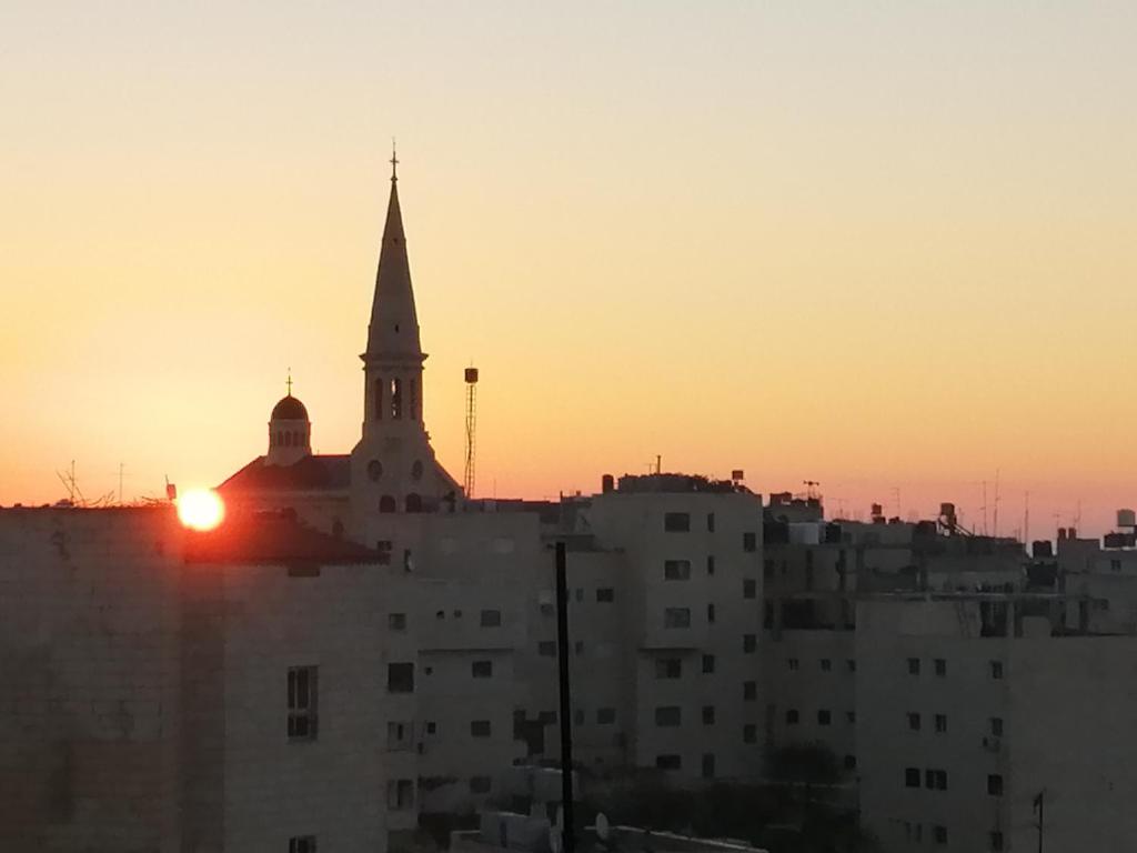 a church steeple with the sun setting behind a city at Bunksurfing Hostel in Bethlehem