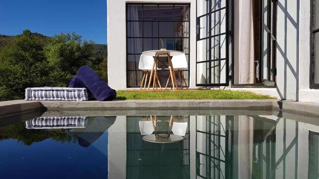 una casa con un reflejo en una piscina de agua en De Kombuys en Oudtshoorn