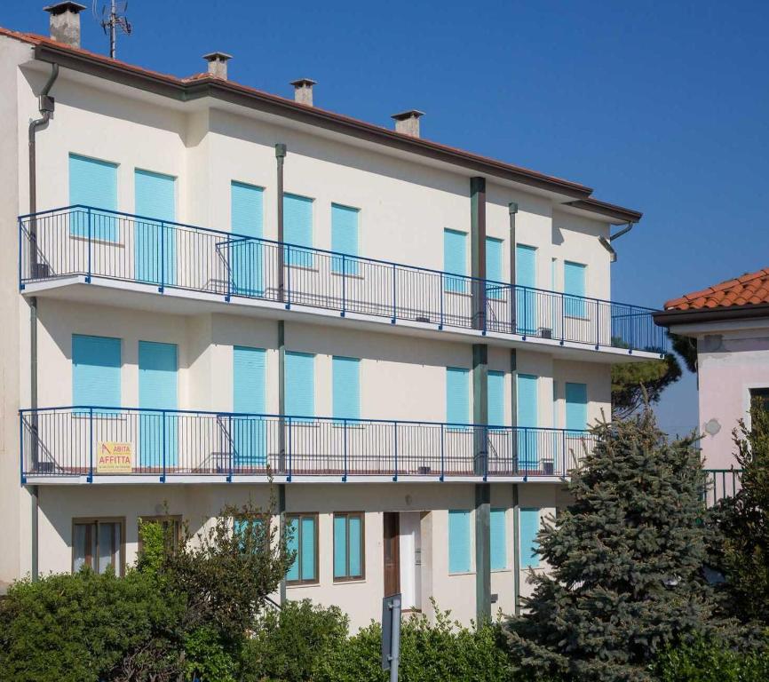 a white building with blue balconies and trees at Residence Cristallo in Caorle