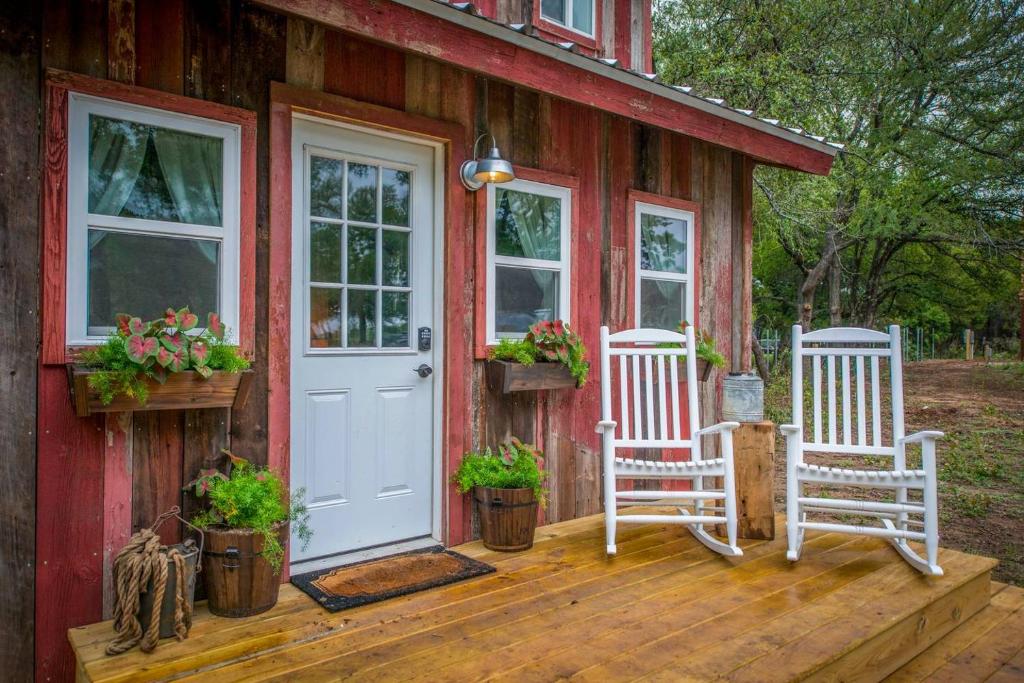 a red house with two white chairs and a door at Cozy Cabin Little Red Hen 12 min to Magnolia in Waco