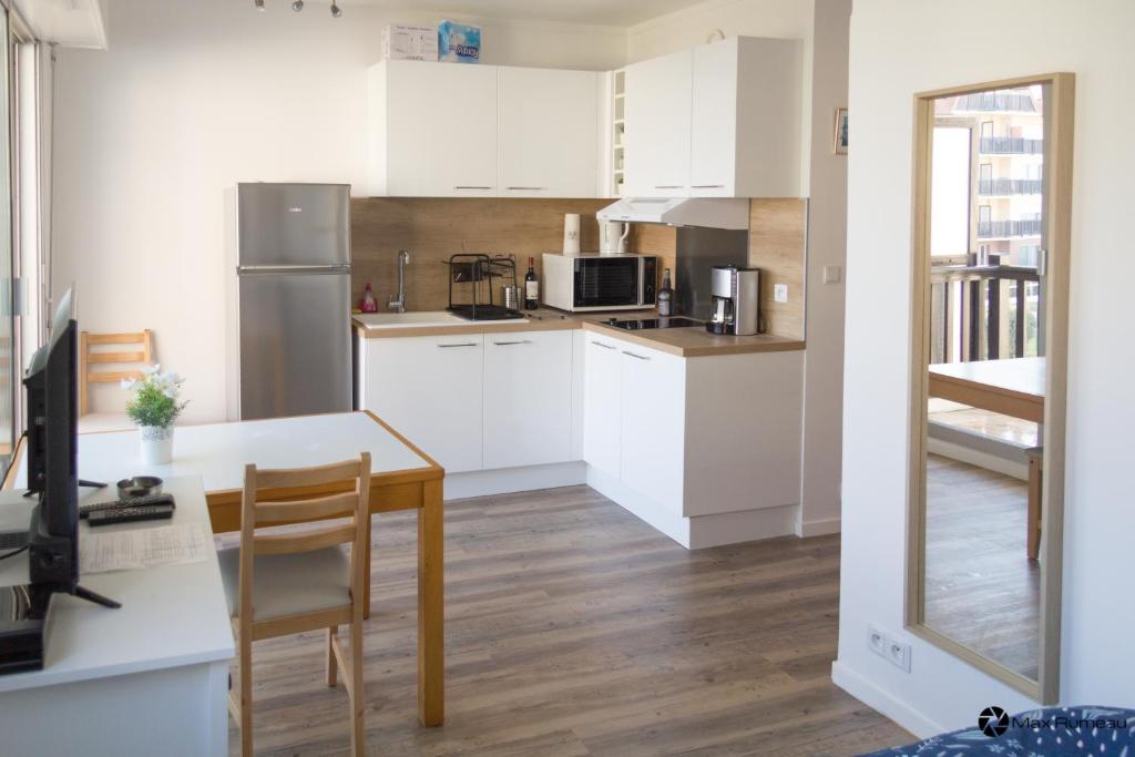 a kitchen with white cabinets and a table and chairs at Studio moderne accès plage, piscine et tennis in Cabourg