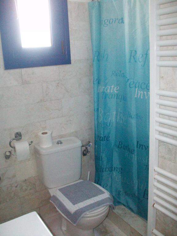a bathroom with a toilet and a blue shower curtain at Serifos Palace in Livadakia
