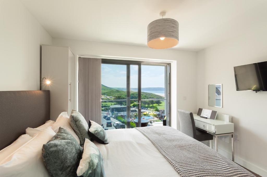 a bedroom with a bed and a desk and a window at 8 Woolacombe West - Luxury Apartment at Byron Woolacombe, only 4 minute walk to Woolacombe Beach! in Woolacombe