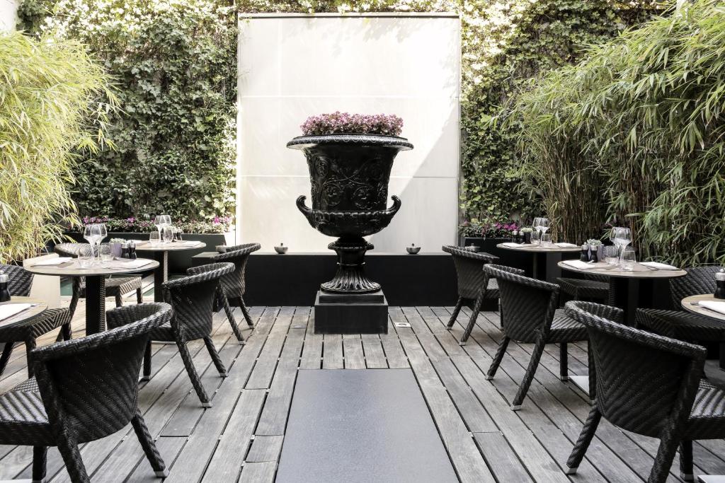 eine Terrasse mit Tischen und Stühlen und eine Vase mit Blumen in der Unterkunft Eastwest Hôtel in Genf