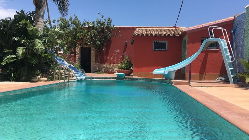 una piscina con un tobogán frente a una casa en HIGOS CHUMBOS, CASA RURAL COMPARTIDO, en Chiclana de la Frontera