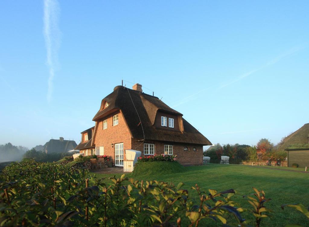 a large house with a thatched roof on a field at Appartementhaus Lüüvhoog in Keitum
