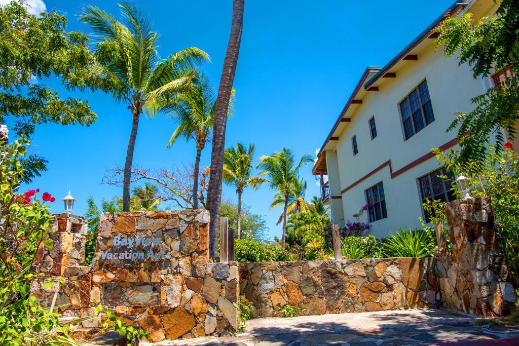 a house with palm trees and a stone wall at Bayview Vacation Apartments in Virgin Gorda