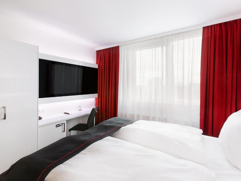 Schlafzimmer mit einem Bett mit roten Vorhängen und einem TV in der Unterkunft DORMERO Hotel Hannover-Langenhagen Airport in Hannover