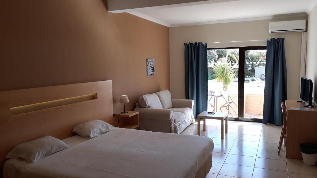 um quarto de hotel com uma cama e uma cadeira e uma janela em Vilamar em Luz