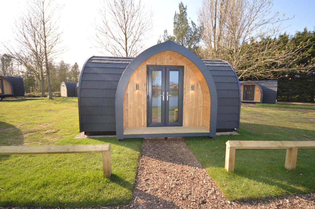 une petite maison dans un champ avec deux bancs dans l'établissement Camping Pods, Birchington Vale Holiday Park, à Birchington