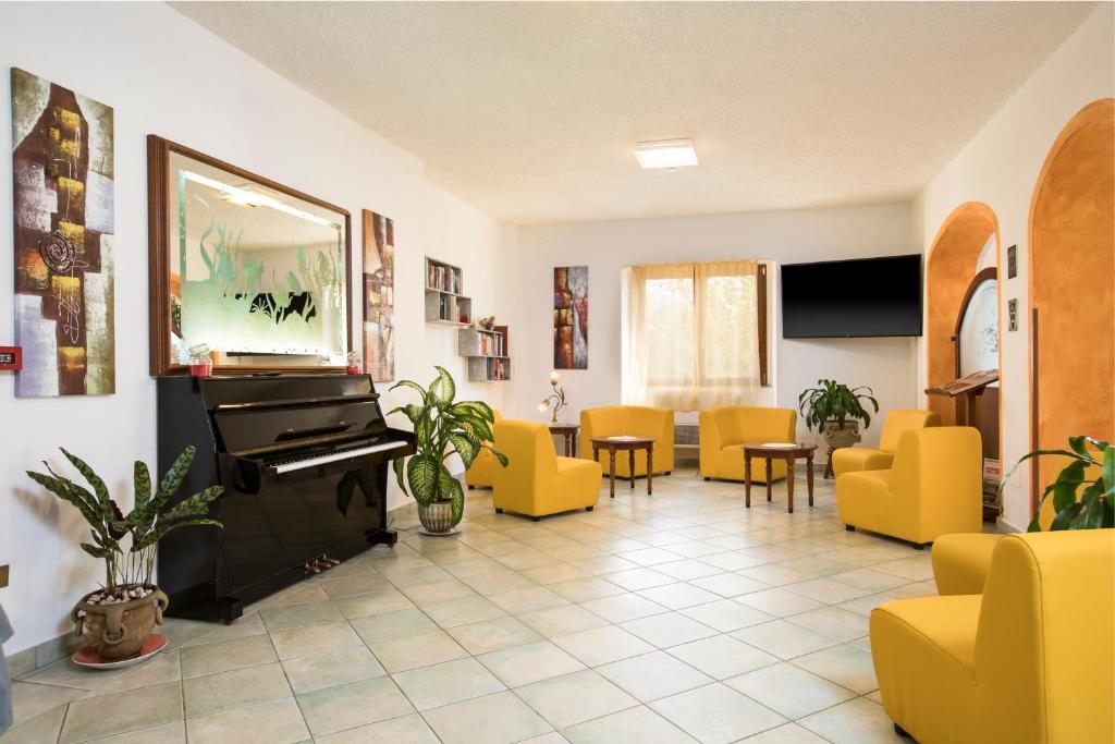 a waiting room with yellow chairs and a piano at Hotel La Playa in Cala Gonone