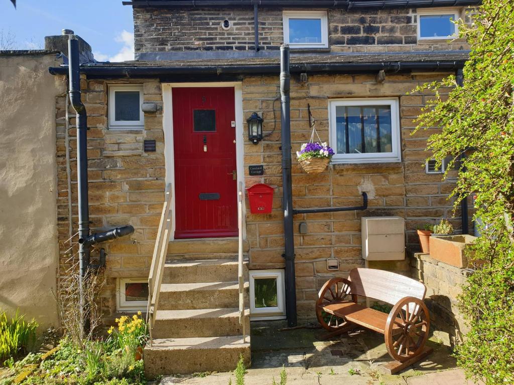 een stenen huis met een rode deur en een bank bij Crosland Cottage in Holmfirth