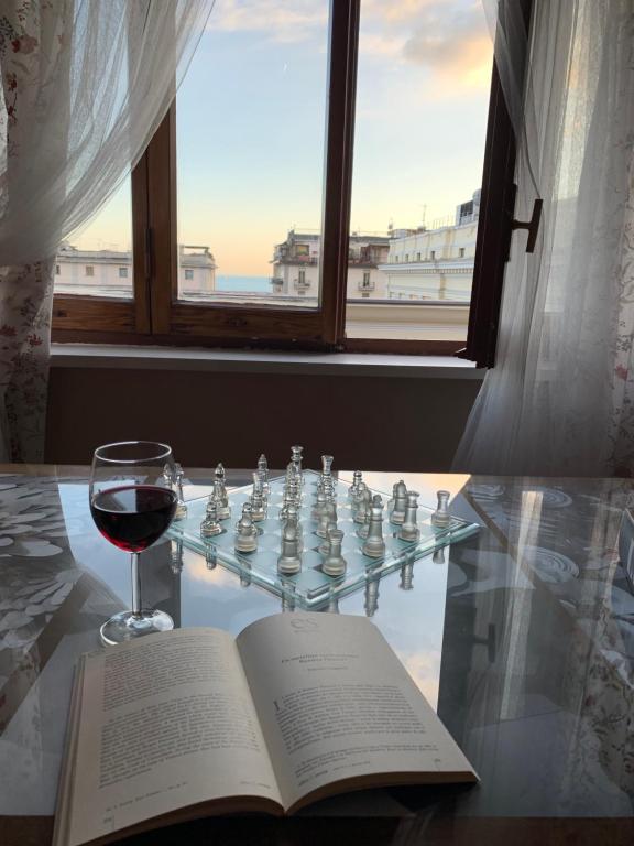 a book and a glass of wine on a glass table with a chessboard at Corso Vittorio Emanuele Luxury house in Salerno