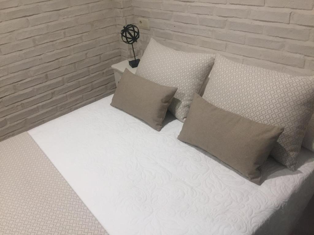 1 cama blanca con almohadas y pared de ladrillo en Ático del Rojas, en Toledo