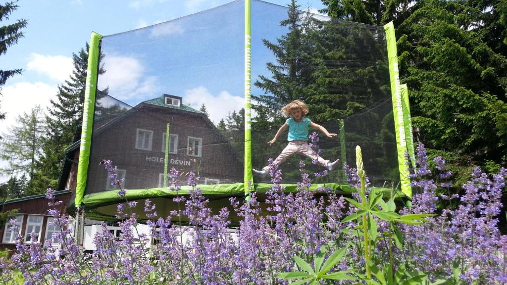 Uma rapariga a saltar num trampolim num jardim com flores roxas. em Hotel Děvín em Pec pod Sněžkou