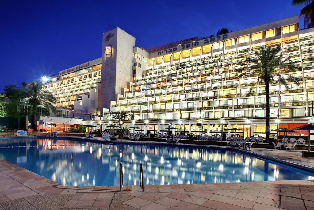 a large building with a swimming pool at night at Club Hotel Tiberias - Suites Hotel in Tiberias