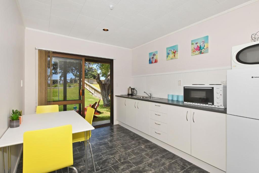 uma cozinha com armários brancos, uma mesa e cadeiras amarelas em Ridge Haven Accommodation em Ruakaka