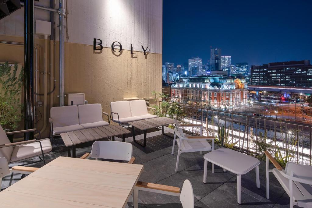 eine Dachterrasse mit weißen Stühlen und Tischen und einer Skyline der Stadt in der Unterkunft THE BOLY OSAKA in Osaka