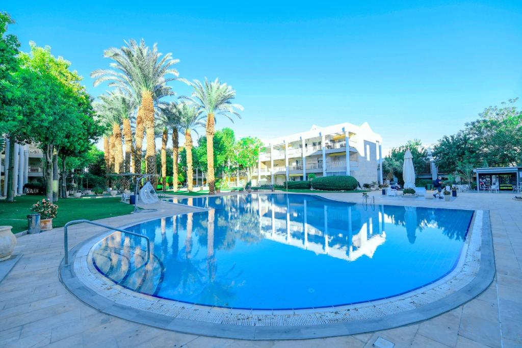 a swimming pool in a park with palm trees and a building at YalaRent Royal Park Resort Complex Apartments in Eilat