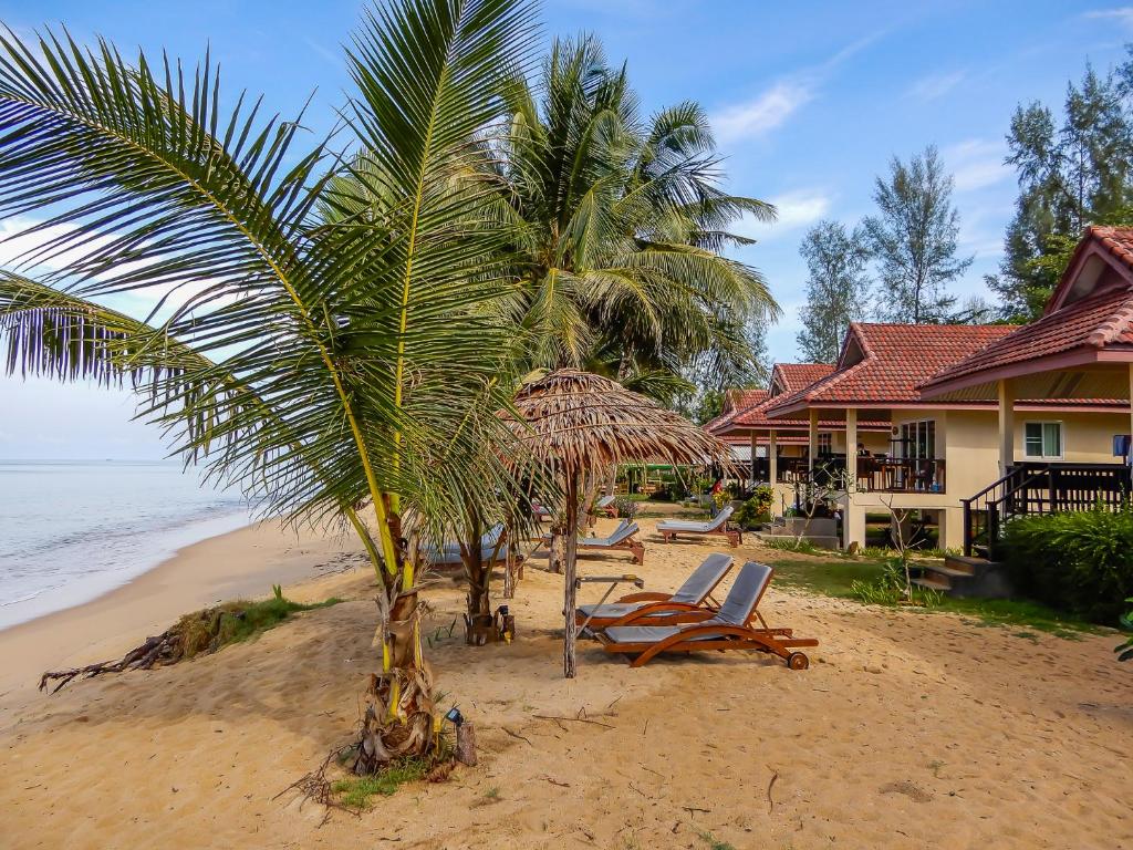 a beach with chairs and a palm tree and a house at Pranee Beach Bungalows in Ko Kho Khao