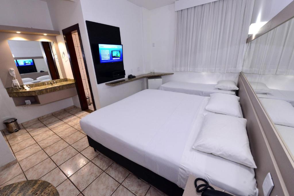 a bedroom with a large white bed and a bathroom at Panorama Tower Hotel in Ipatinga