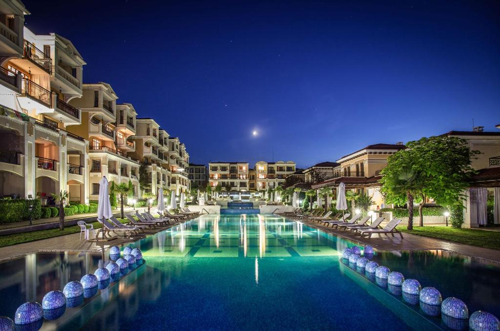 a swimming pool with chairs and buildings at night at Green Life Apartments Sozopol in Sozopol