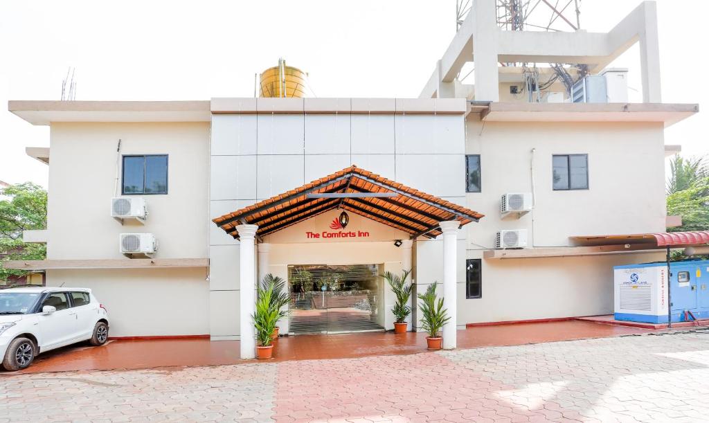 门格洛尔Treebo Comforts Inn, University Road Deralakatte的一栋白色建筑，前面停着一辆汽车