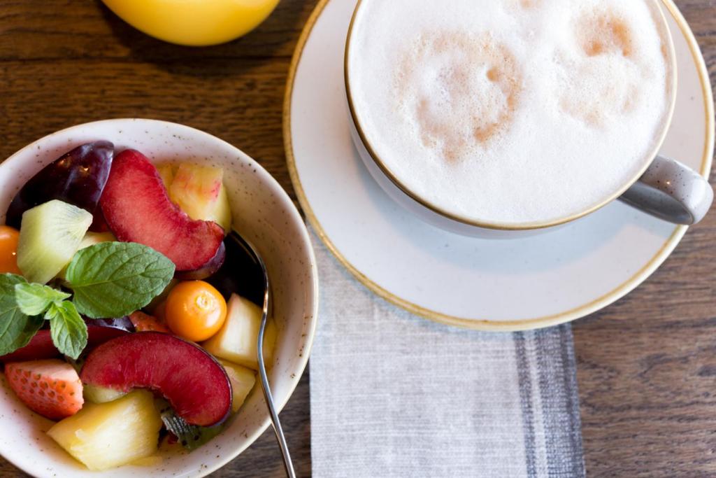 a bowl of fruit next to a cup of coffee at Hotel Neptun in Warnemünde