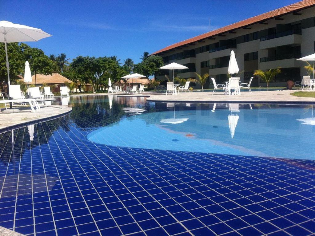 uma piscina com cadeiras e guarda-sóis ao lado de um hotel em Carneiros Beach Resort apto 208A em Praia dos Carneiros