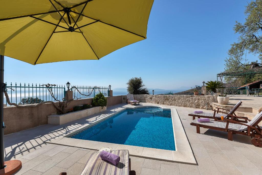 a swimming pool with a yellow umbrella and chairs at Villa Ana in Podgora