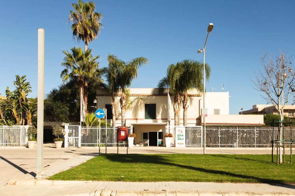 una valla frente a un edificio con palmeras en Hotel Baia Del Sole, en Marina di Ragusa