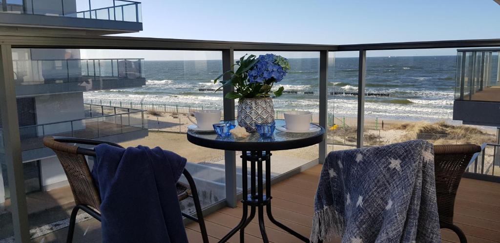 a table with a vase of flowers on a balcony with the beach at Apartament MorSky Gardenia Dziwnów in Dziwnów