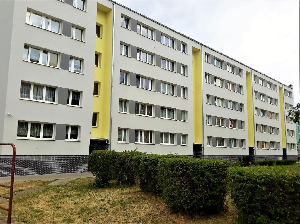 a white and yellow building with bushes in front of it at Apartament Słoneczny in Świnoujście