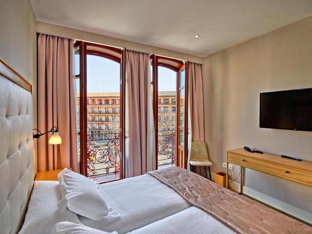 トレドにあるHotel Boutique Adolfoのベッドと大きな窓が備わるホテルルームです。