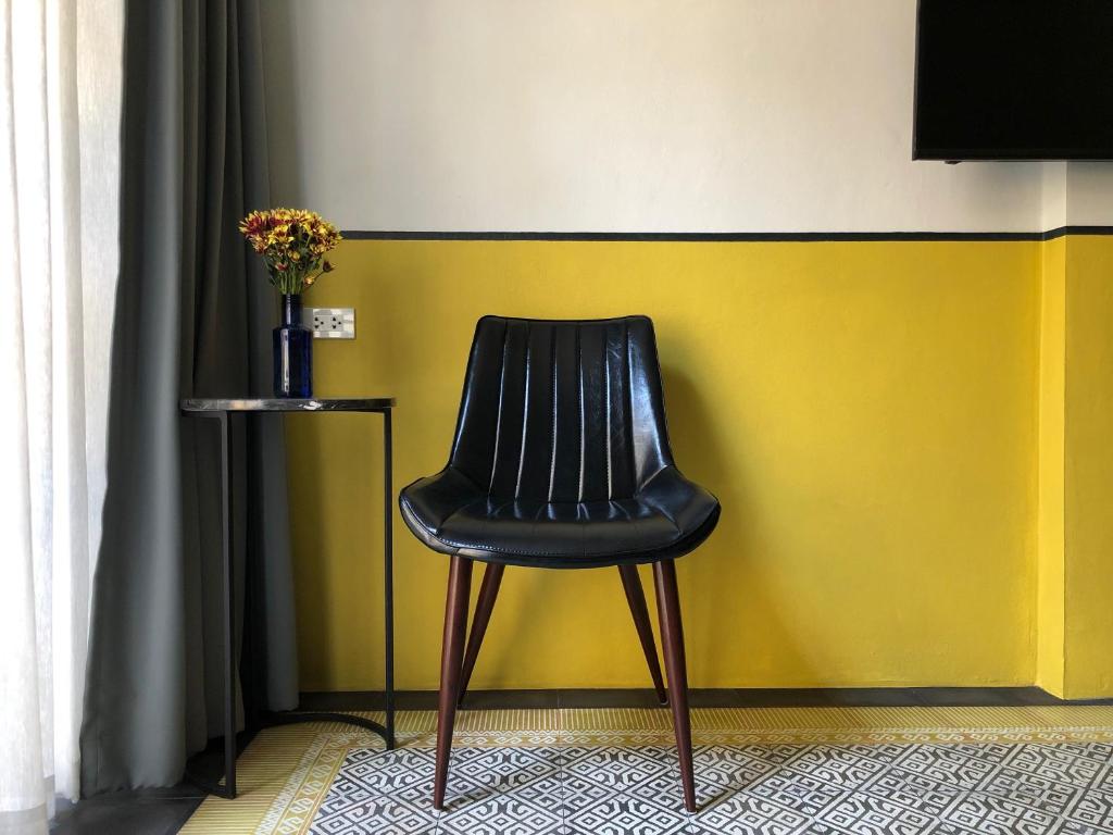 ハジャイにあるGoodnight Poshtel + Free Netflixの黄色い壁の前に座る黒い椅子