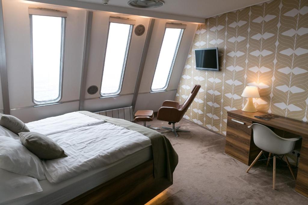 a bedroom with a bed and a desk and windows at Hotel Ještěd in Liberec