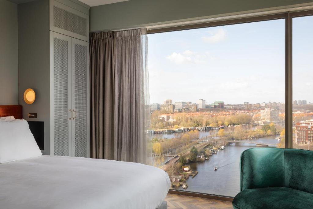 een slaapkamer met een groot raam met uitzicht op een rivier bij Olympic Hotel in Amsterdam