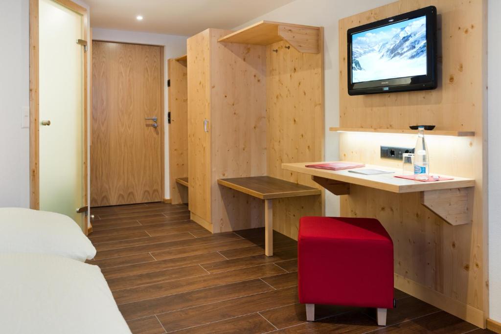 a room with a desk and a tv on a wall at Hotel Caprice - Grindelwald in Grindelwald