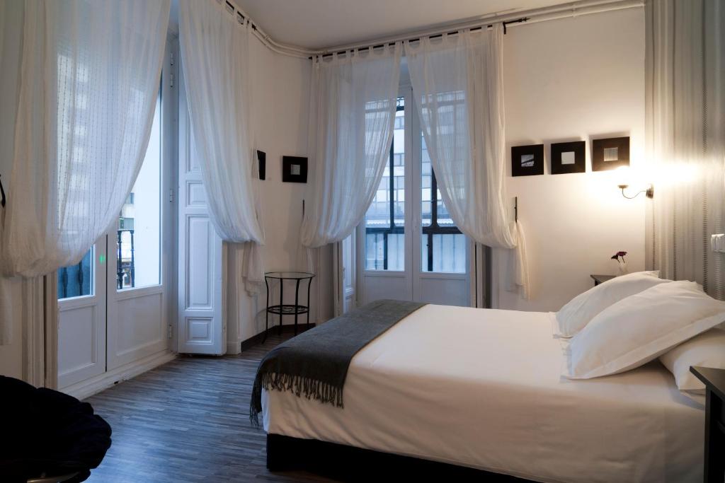 a bedroom with a bed with white sheets and windows at Hostal Gala Madrid in Madrid