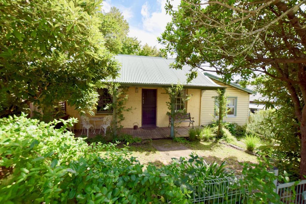 a yellow house with a porch and trees at Waragil Cottage - Original Settler's Home in Blackheath