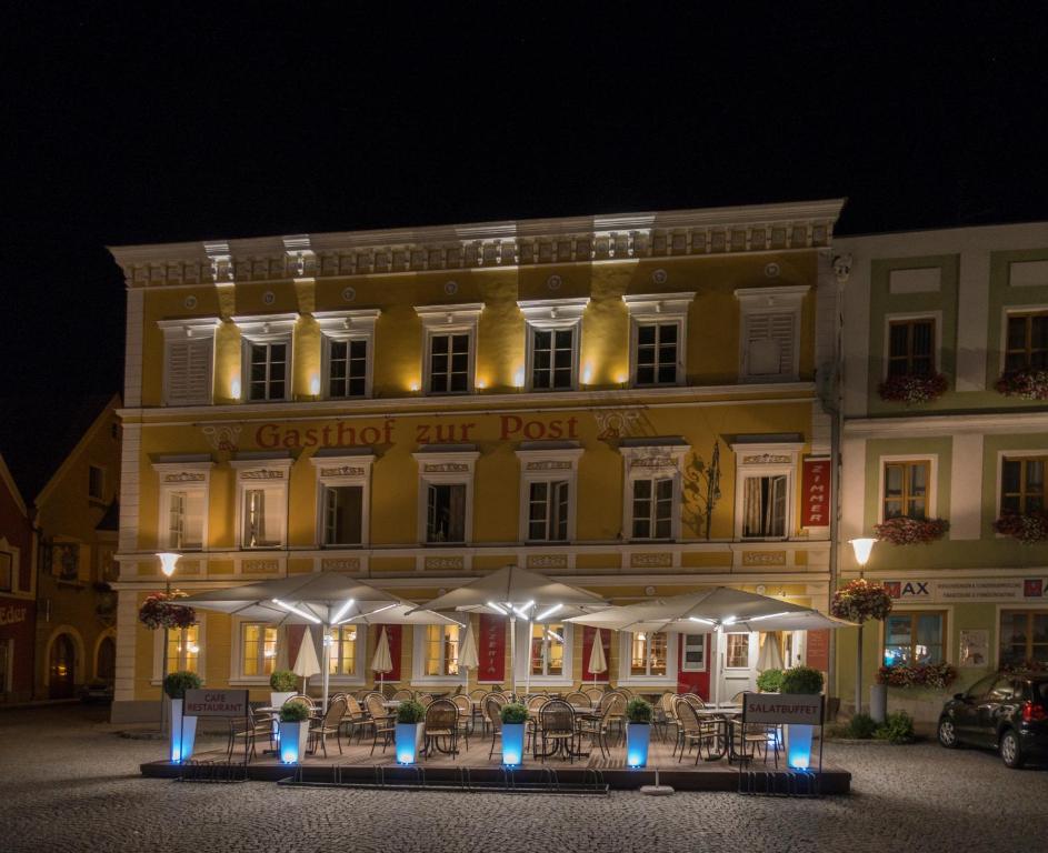 um grande edifício amarelo com mesas e guarda-chuvas brancos em Hotel Gasthof zur Post em Obernberg am Inn