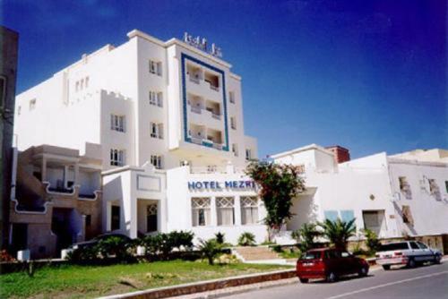 莫納斯提爾的住宿－梅茲裡酒店，前面有一辆汽车停放的白色建筑