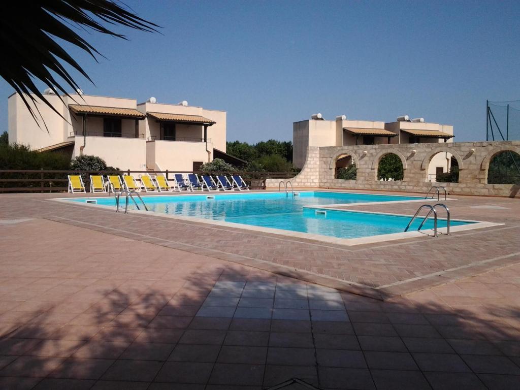 a swimming pool with lounge chairs in front of a building at Residence Punta Longa in Favignana