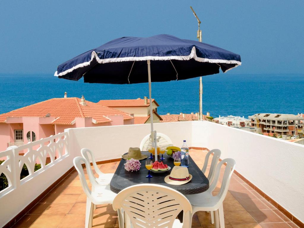 einen Tisch mit einem blauen Sonnenschirm auf einem Balkon mit Meerblick in der Unterkunft Villa Vila Hortencia by Interhome in Ericeira