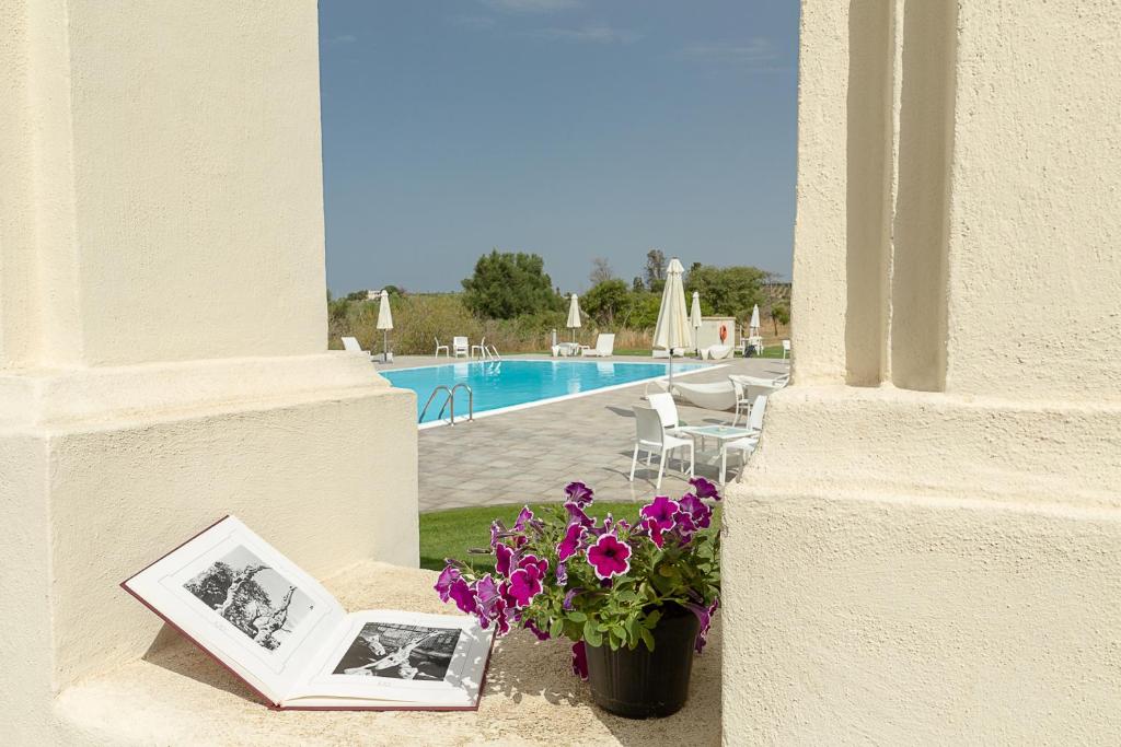 un libro y flores sentados en una cornisa junto a una piscina en Hotel Villa Calandrino, en Sciacca